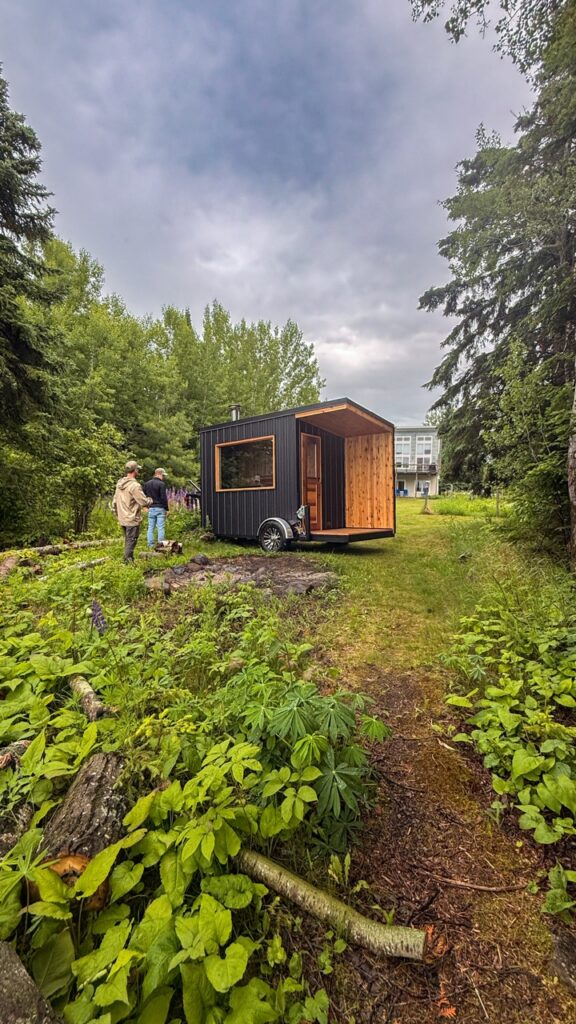 Black mobile sauna trailer with cedar changing porch parked on grass