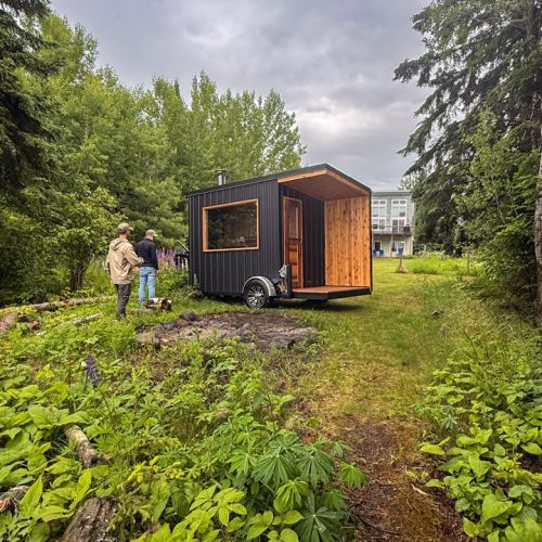 Black mobile sauna trailer with cedar changing porch parked on grass